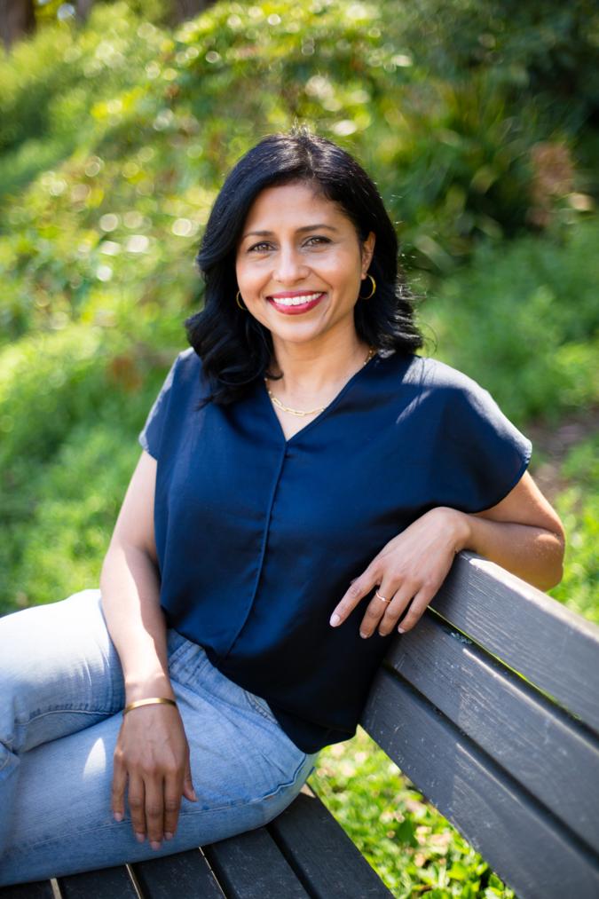 Shantal De Silva, licensed Speech-Language Pathologist, seated on a garden bench and smiling