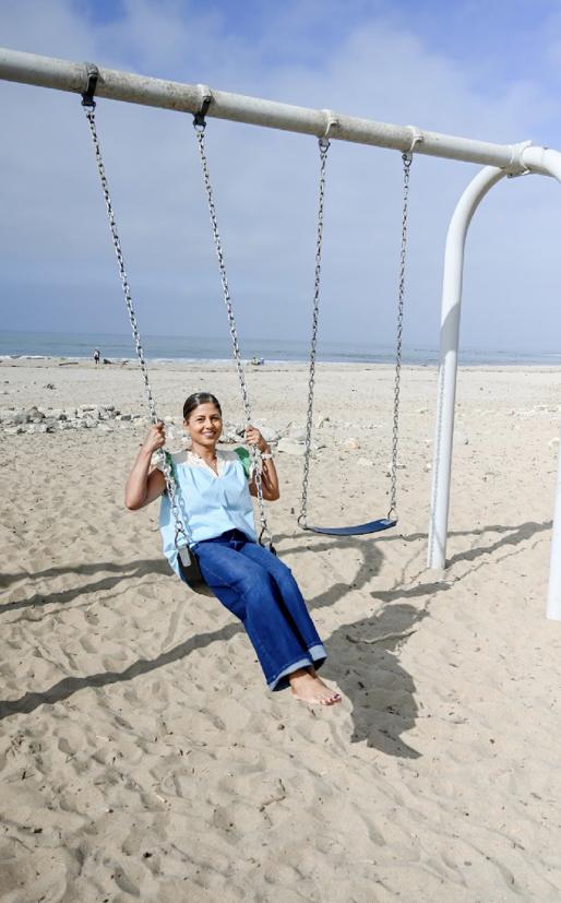 Shantal laughing on a beach swing with the ocean behind her