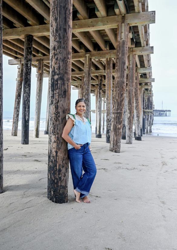 Shantal leaning against a weathered piling beneath a wooden pier at the beach